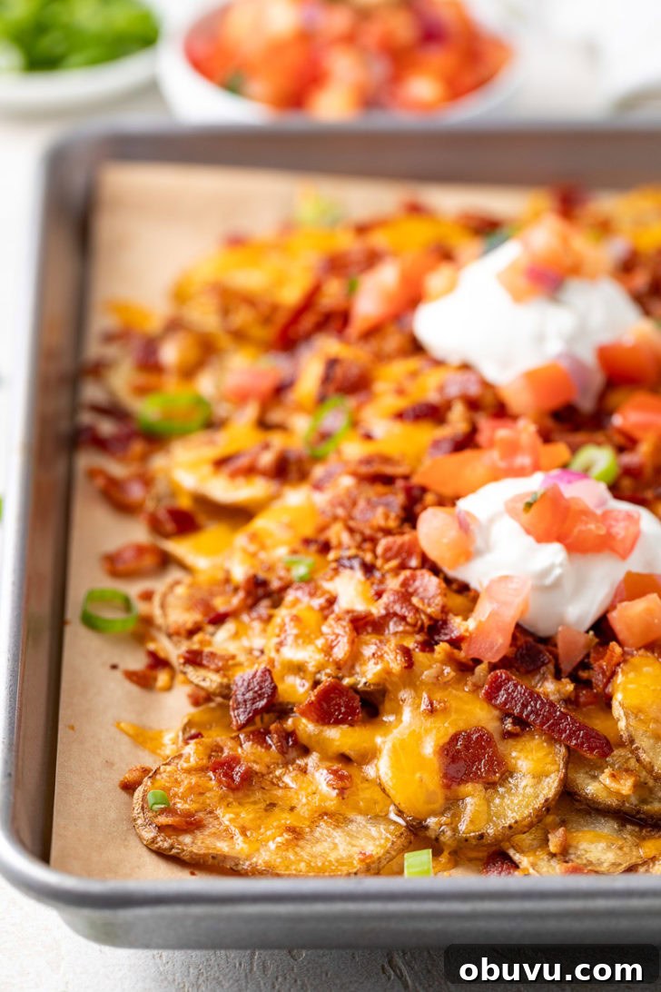 Loaded Potato Nachos with Cheese, Jalapeño & Sour Cream 4 A close-up of crispy baked potato nachos topped with sour cream, diced tomatoes, and bacon.