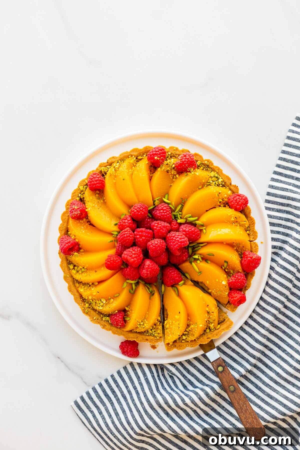 Slicing a pistachio tart topped with raspberries and peaches.