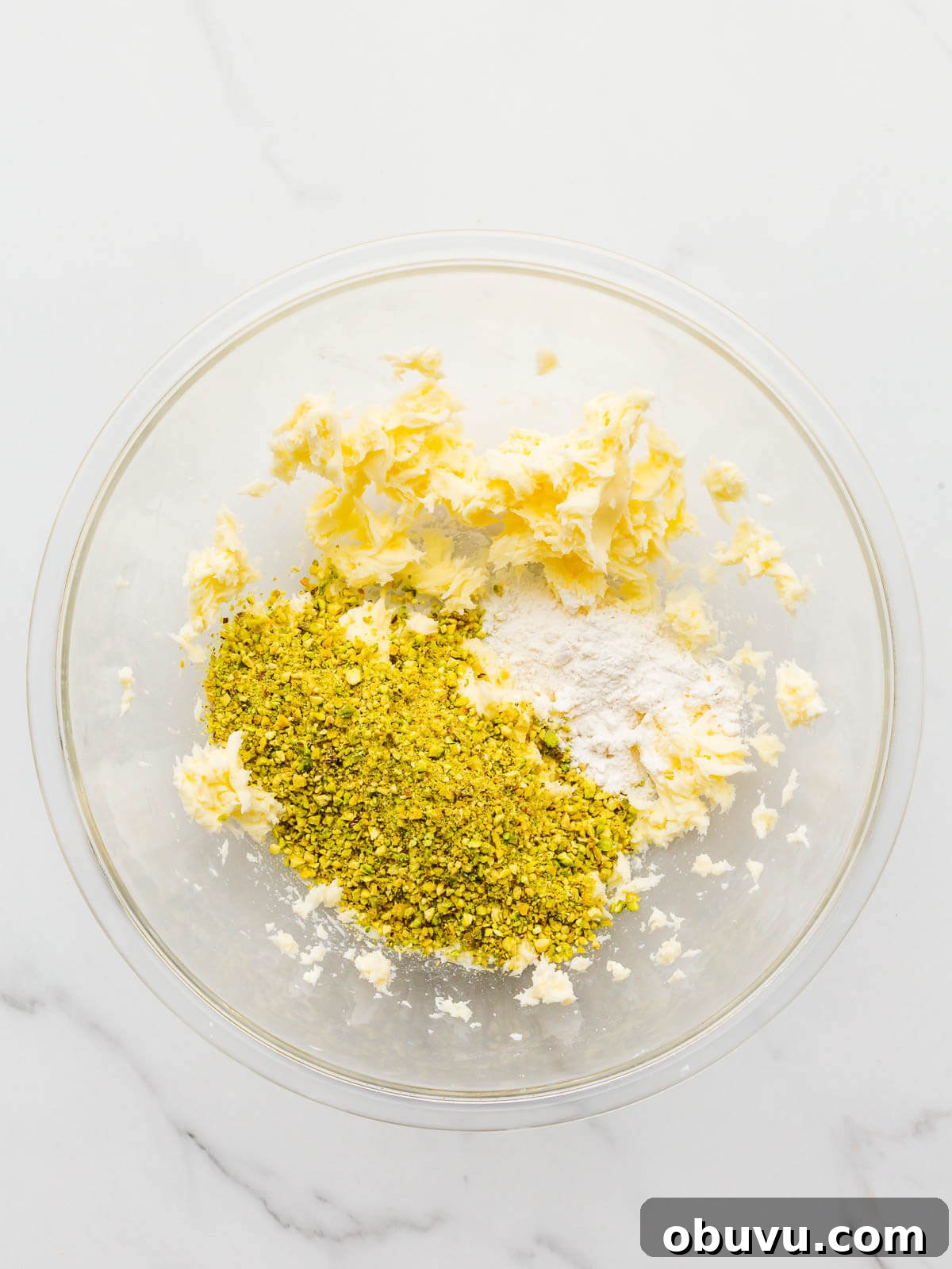 Adding ground pistachios to a bowl to make a pistachio cream filling for a tart.