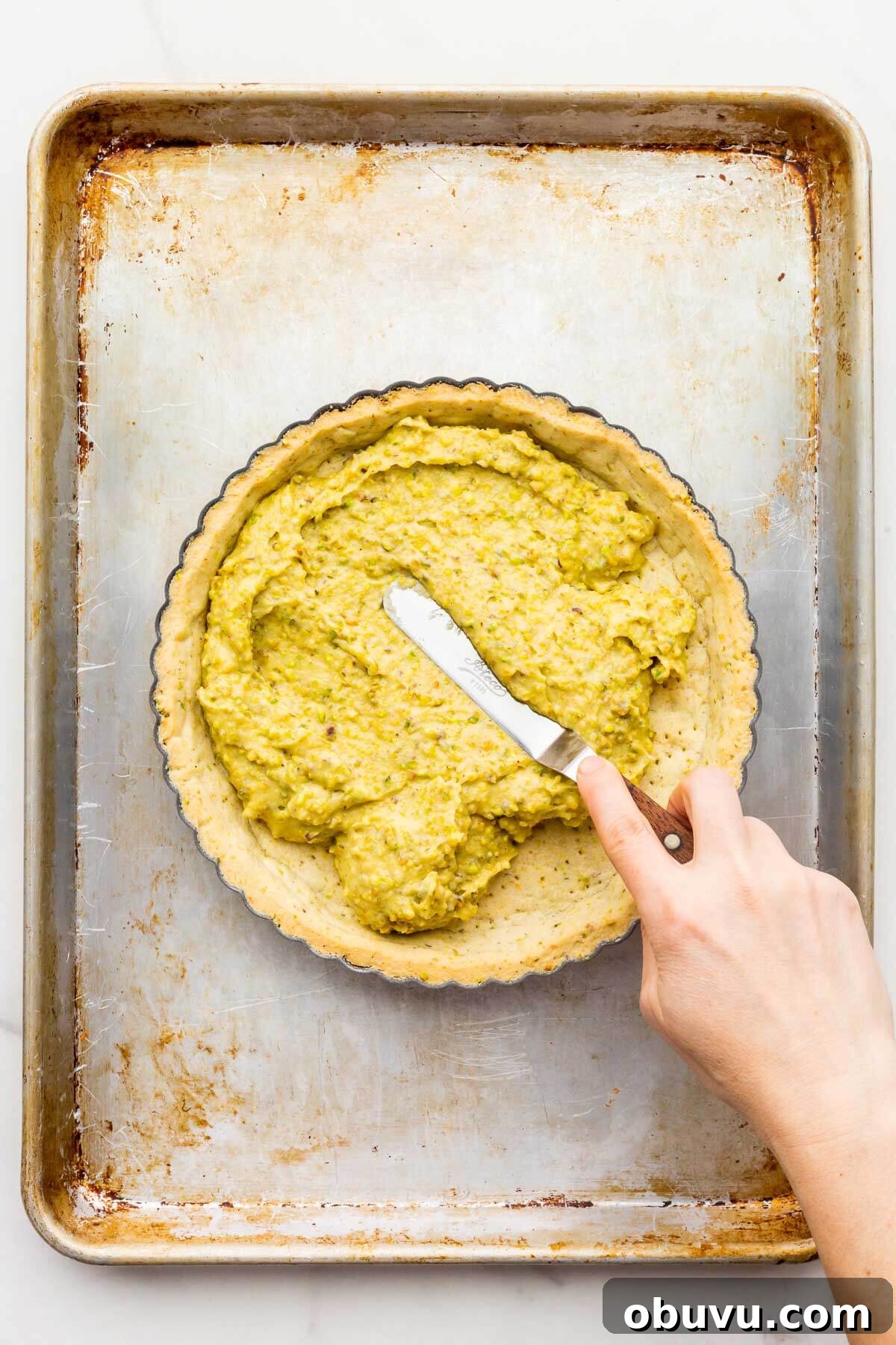 Spreading a pistachio cream filling over a baked pistachio crust with an offset spatula to make a tart.