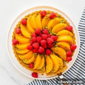 Slicing and serving a pistachio tart topped with sliced peaches and fresh raspberries, and decorated with slivered and ground green pistachios.
