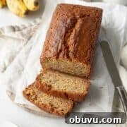 Moist Banana Bread Without Gluten — Simple Recipe for Tasty Loaf 4 A sliced loaf of gluten free banana bread on sheets of parchment paper and a knife laying next to it.