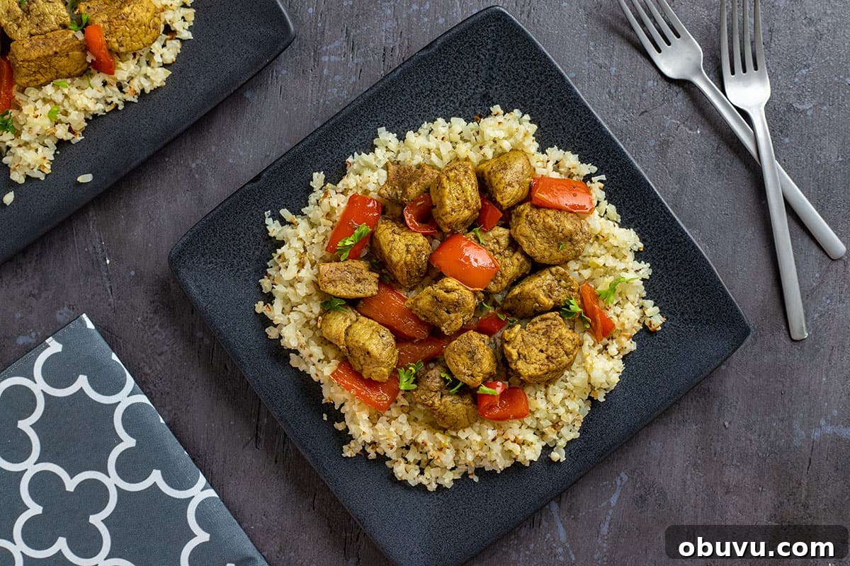 Keto Pork Curry with Cauliflower Rice Bowl 6 cooked pork curry on top of cauliflower rice in square black plate with forks and gray napkin
