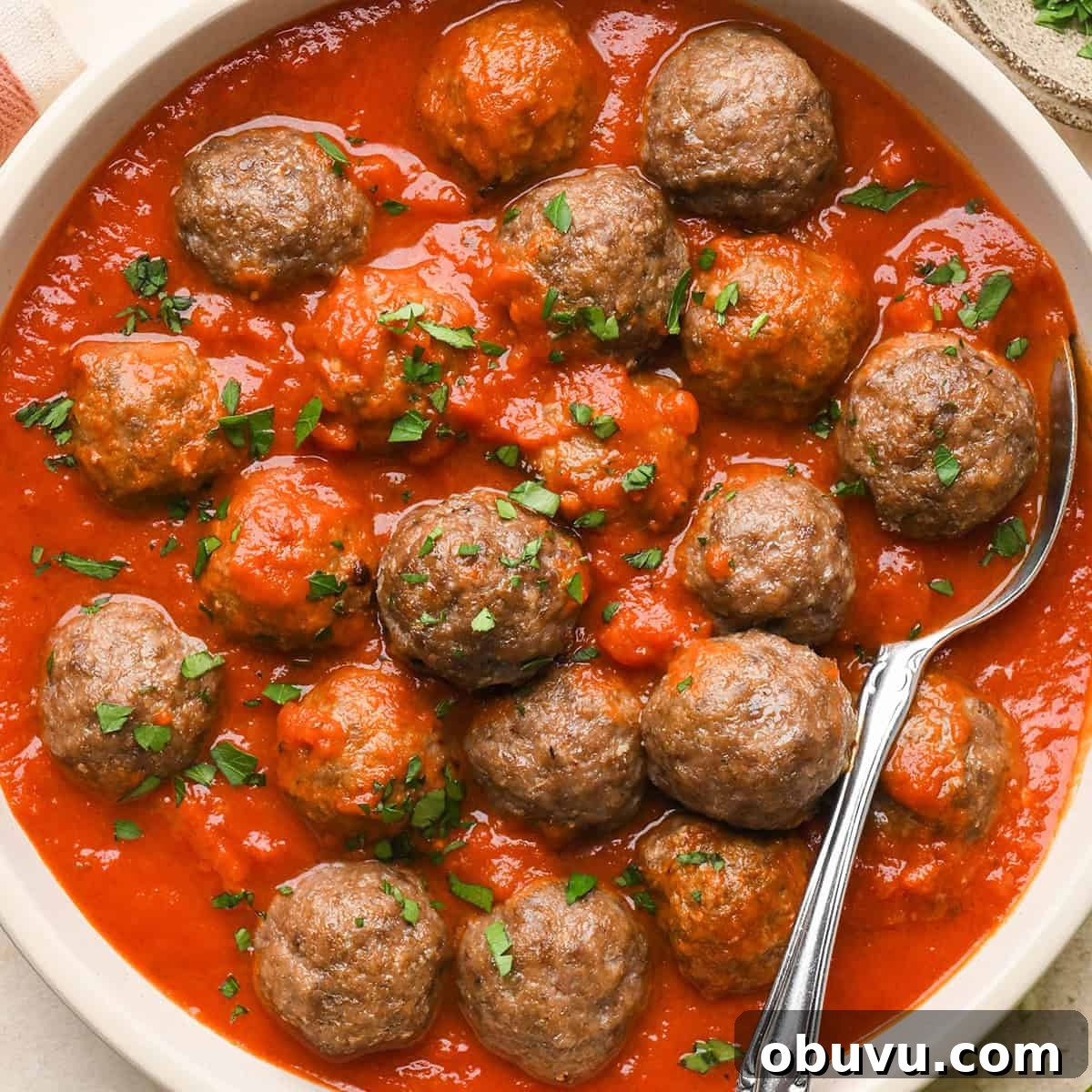 Gluten-Free Italian Meatballs Recipe – Tender & Flavorful 18 Gluten Free Meatballs garnished with basil in a bowl in marinara sauce with a spoon.