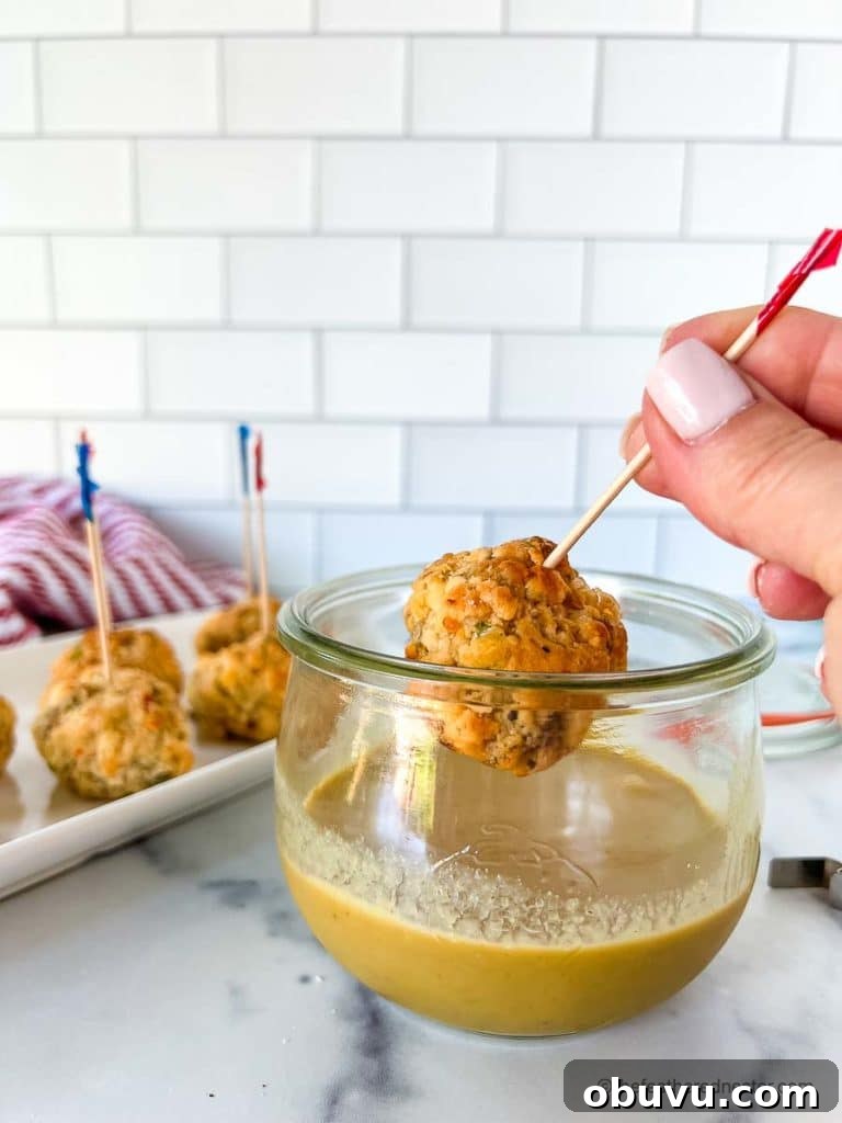 appetizer toothpick stuck in a meatball made from palmetto cheese balls with a dipping sauce in the background