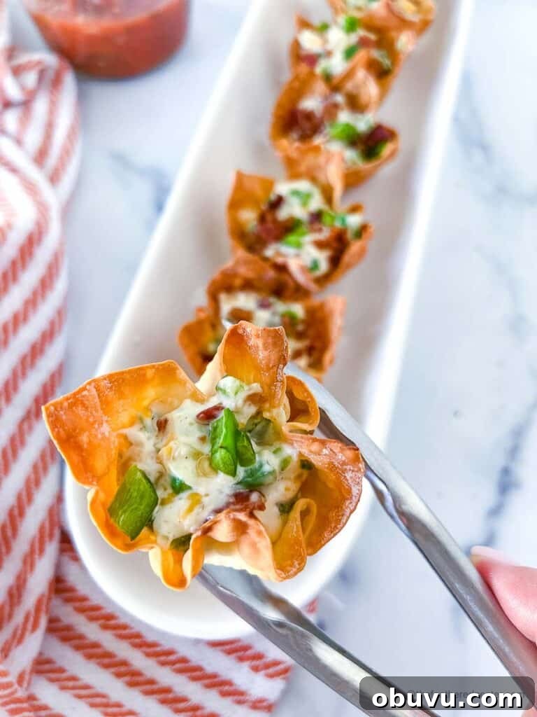 a hand and tong holding a jalapeno popper wonton cup and a serving tray full of jalapeno wonton popper cups
