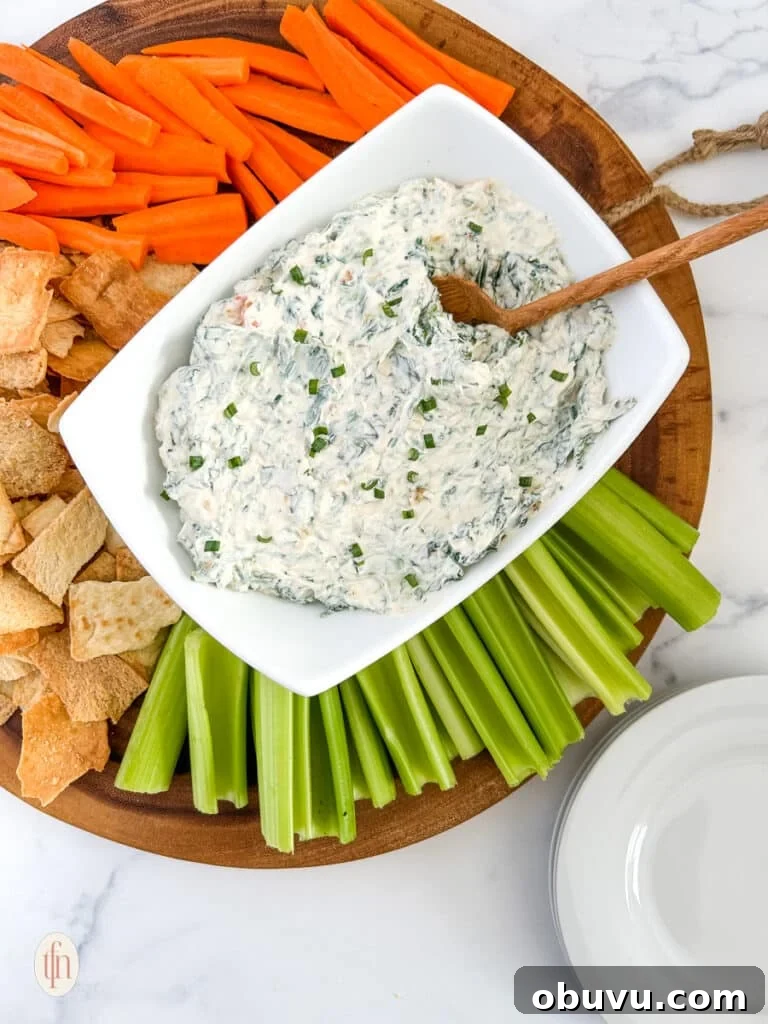 Knorr spinach dip on a serving rectangular bowl with a wooden spoon. Served on top of a round wooden board with crackers and vegetables.