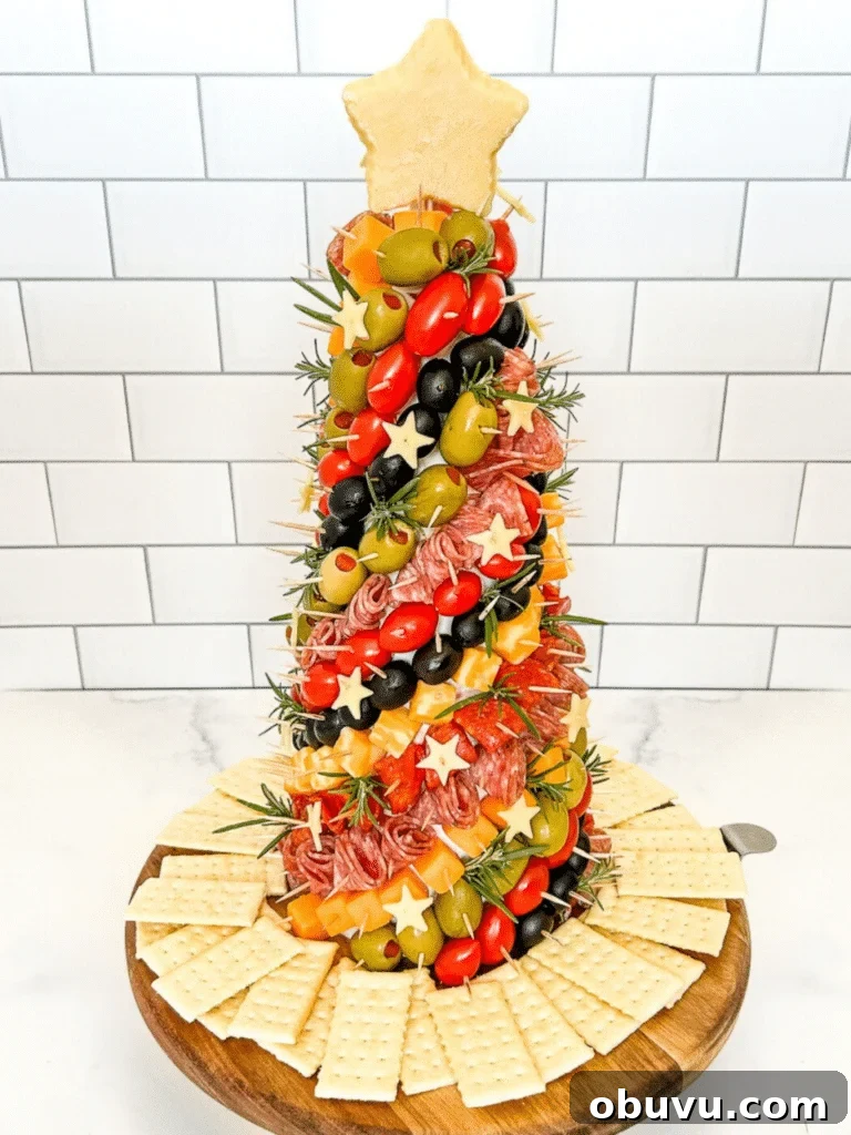 Decorated charcuterie tree standing vertically on a platter with a white background.