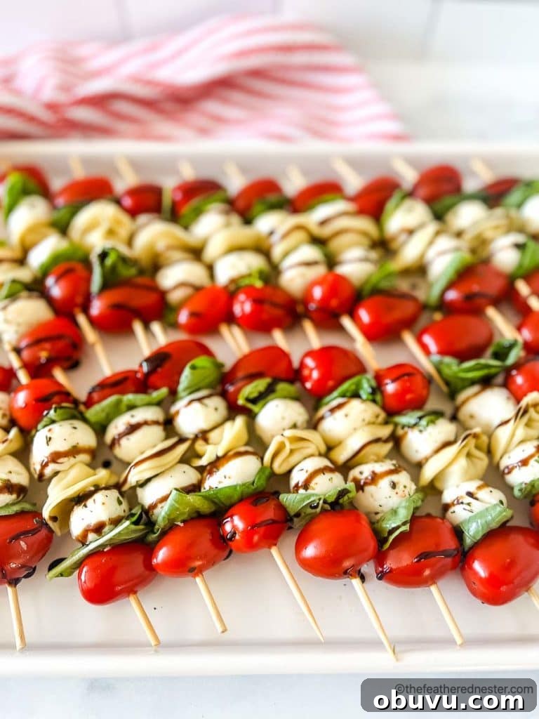 a white tray of tortellini skewers with balsamic glaze on top of a red and white napkin.
