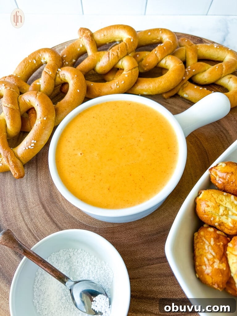 A serving bowl of pretzel cheese dip next to pretzels and a bowl of salt.