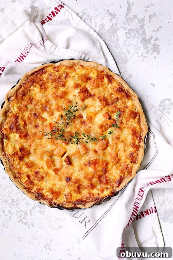 Photo of whole Butternut Squash Leek and Gruyere Tart on white printed towel garnished with fresh thyme.