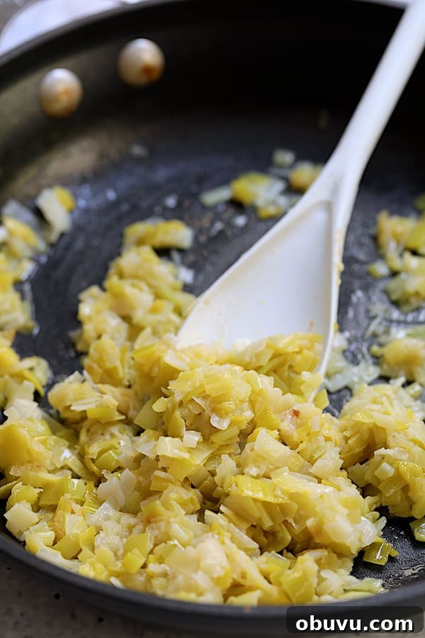 Photo of leeks being sauteed in nonstick skillet and being stirred with white spoon.