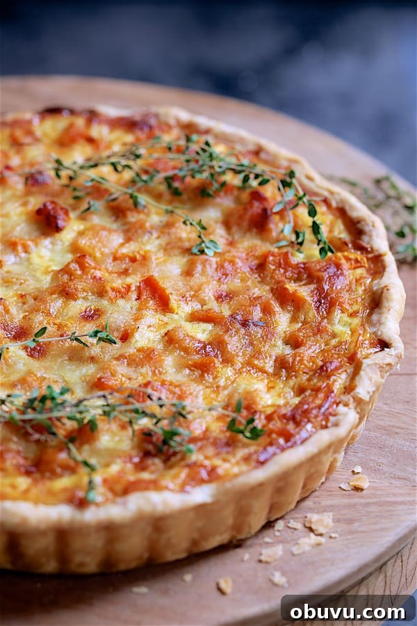 Close-up photo of whole Butternut Squash Leek and Gruyere Tart on wood stand garnished with fresh thyme.