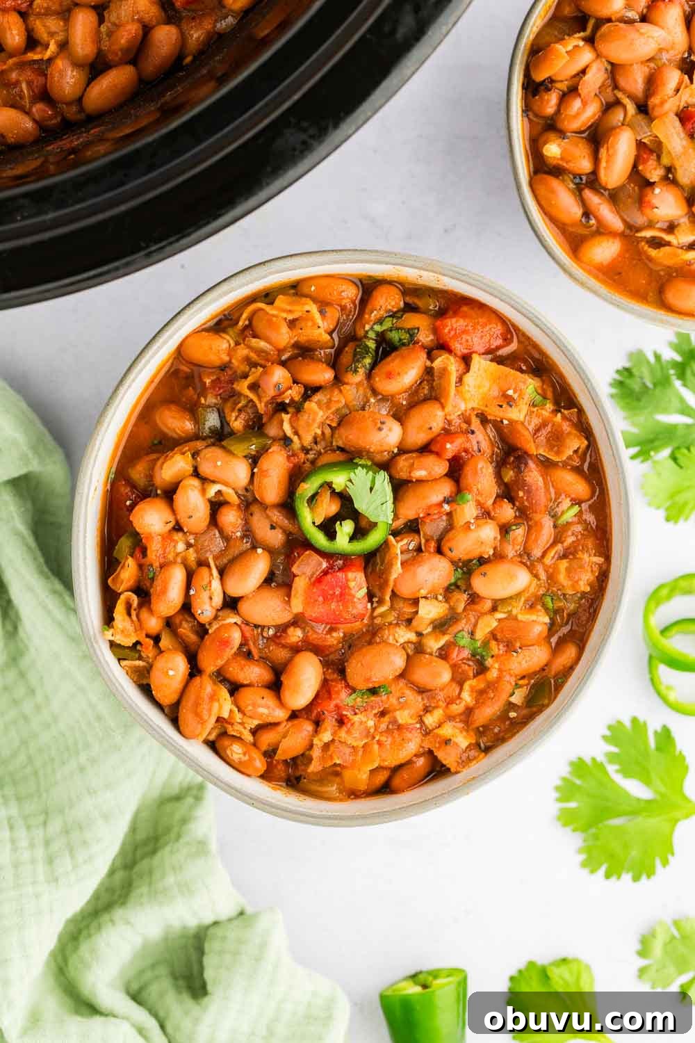 Charro Beans served in bowl garnished with jalapeño next to slow cooker