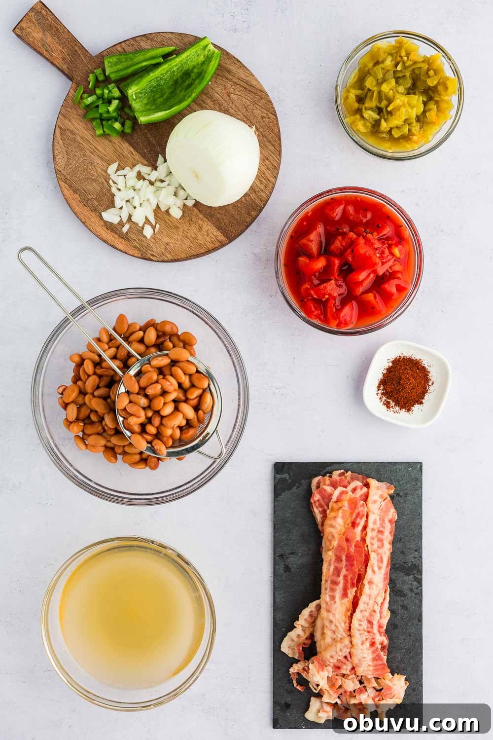 Various ingredients like broth, bacon, beans, onion, peppers, tomato, and seasonings displayed on table