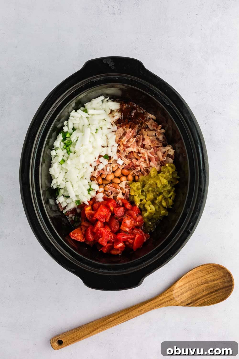 4 cans pinto beans 2 oz packaged pre-cooked bacon 14.5 oz can fire-roasted diced tomatoes 2 oz canned diced green chilis 1 jalapeno pepper, seeded and diced 1 medium yellow onion, diced (about 1 cup) 2 teaspoons homemade chili seasoning 2 cups chicken broth all in slow cooker next to wooden spoon