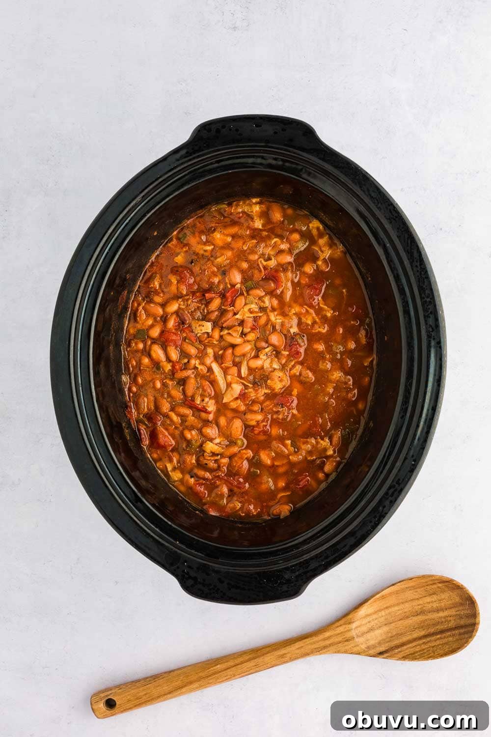 4 cans pinto beans 2 oz packaged pre-cooked bacon 14.5 oz can fire-roasted diced tomatoes 2 oz canned diced green chilis 1 jalapeno pepper, seeded and diced 1 medium yellow onion, diced (about 1 cup) 2 teaspoons homemade chili seasoning 2 cups chicken broth mixed to make charro beans in slow cooker next to wooden spoon