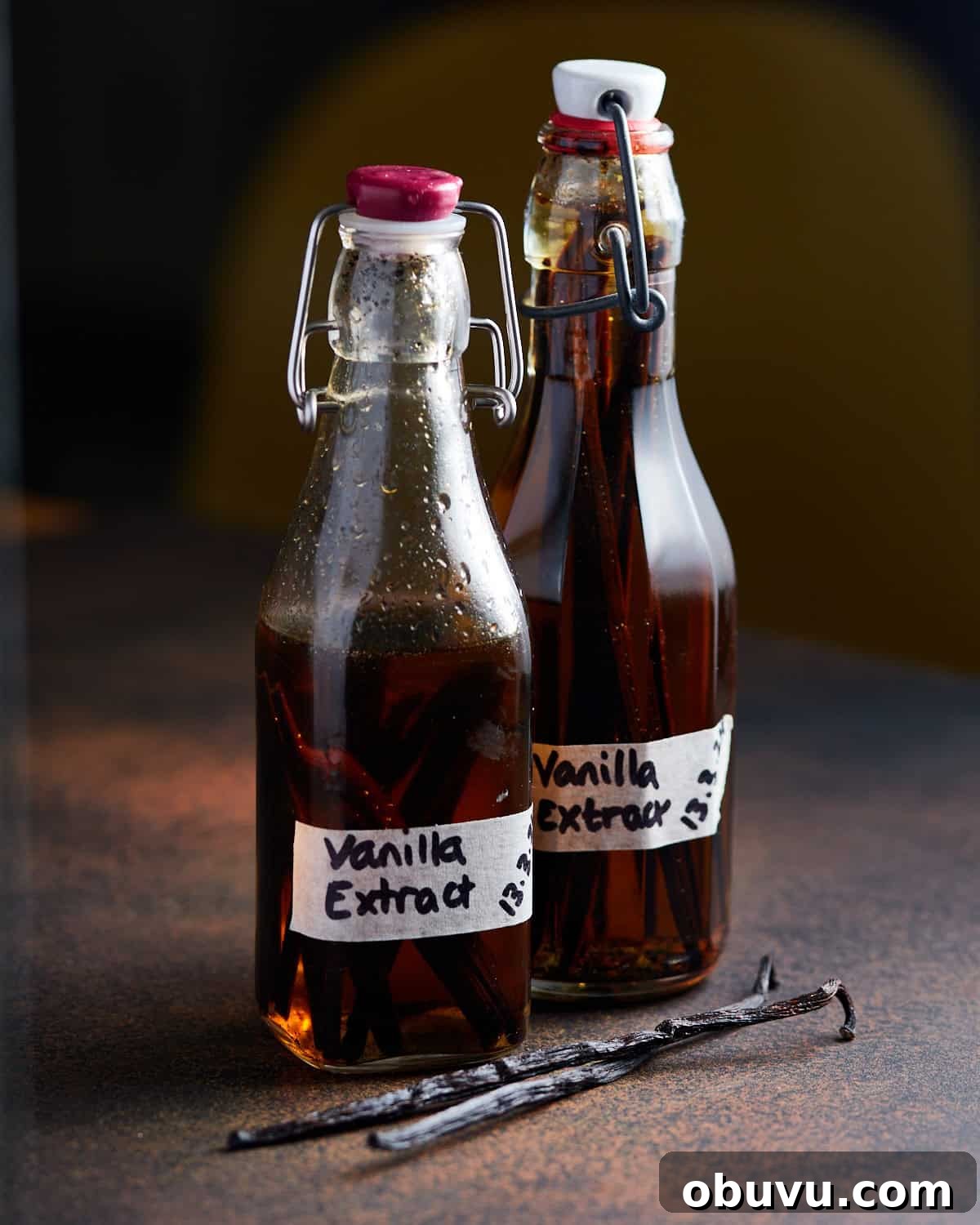 Alcohol-Free Homemade Vanilla Extract Recipe 7 Photo of two small bottles of homemade vanilla extract on a dark worktop with two vanilla pods lying in front.