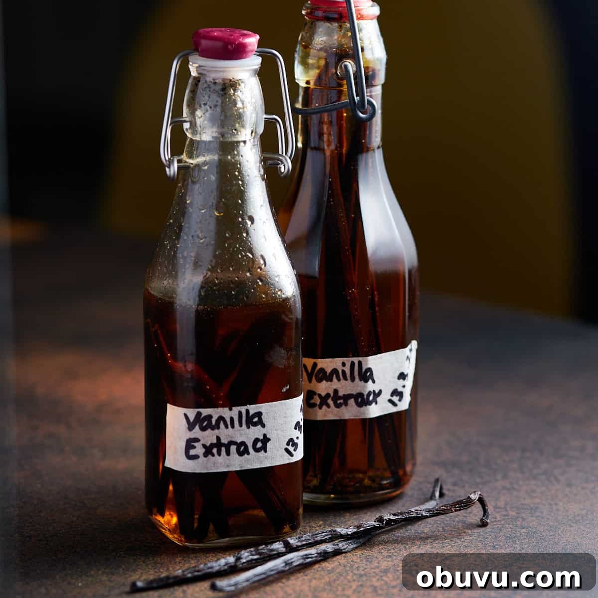 Alcohol-Free Homemade Vanilla Extract Recipe 9 Square photo of two small bottles of homemade vanilla extract on a dark worktop with two vanilla pods lying in front.