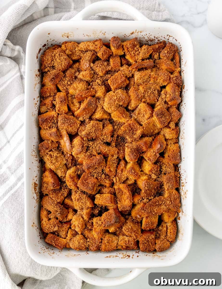 Overnight Brioche French Toast Casserole Recipe 9 Baked dish of golden brown bread cubes in a white rectangular casserole dish, placed on a marble surface with a striped cloth nearby.