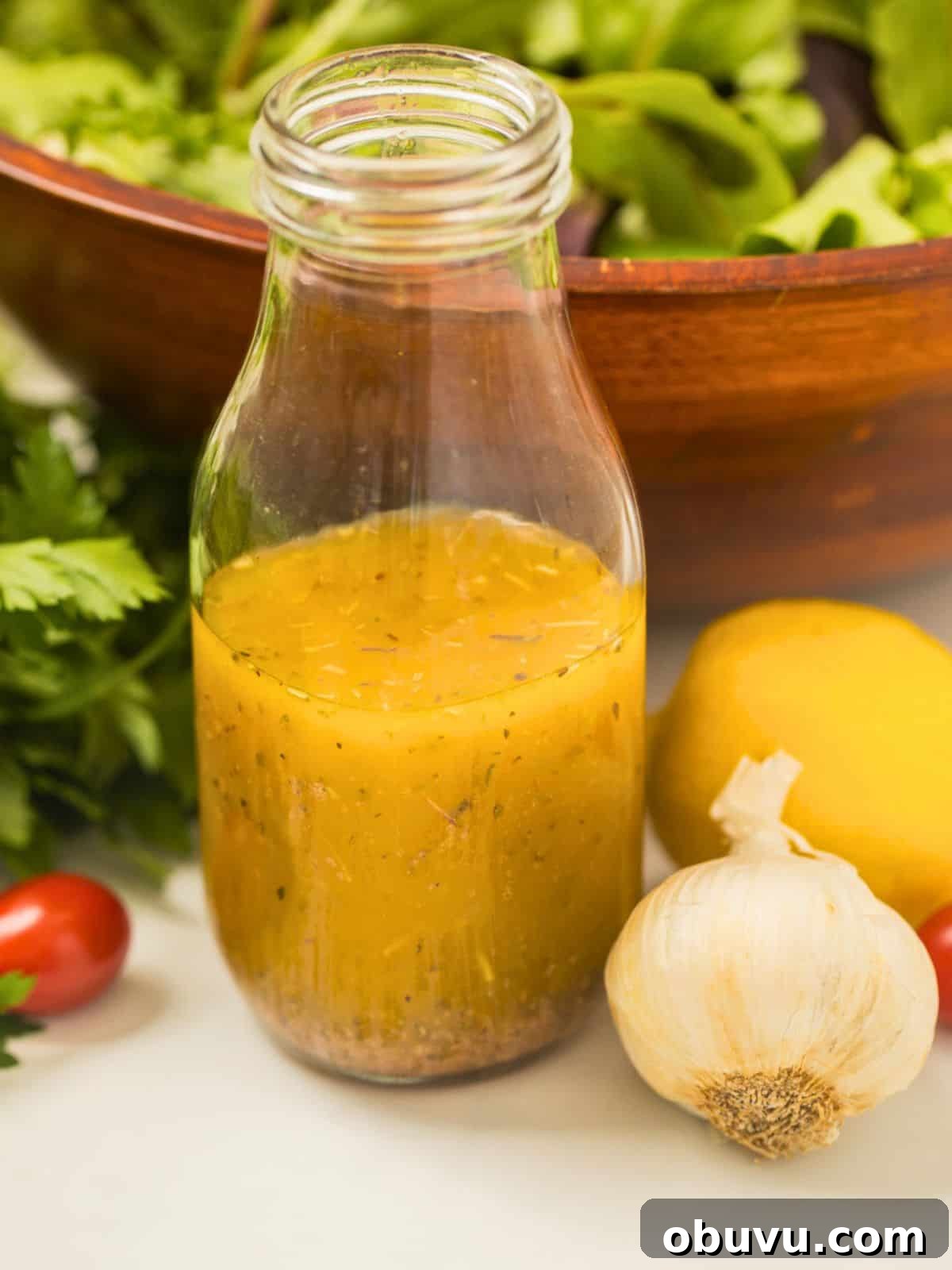 Bottle of homemade zesty Italian dressing next to garlic and a tossed salad.
