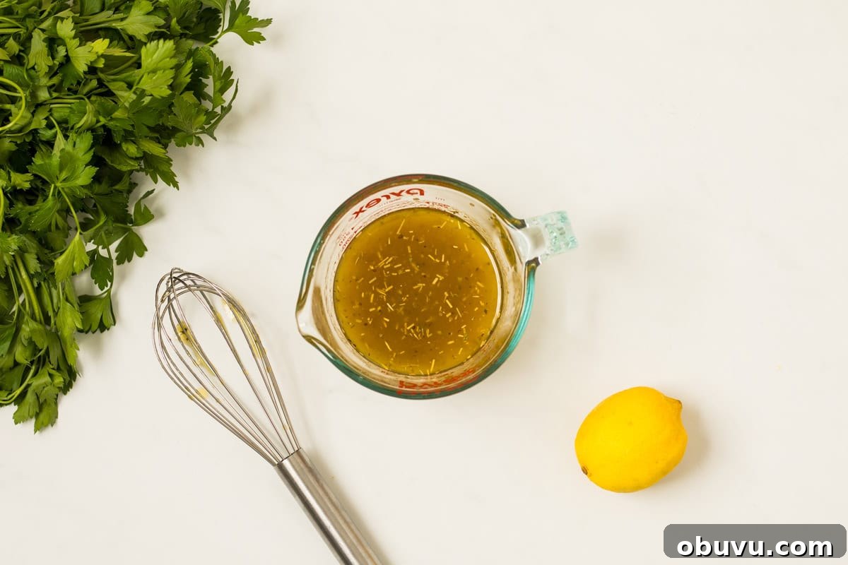 Italian dressing whisked together in glass measuring cup next to fresh lemon.