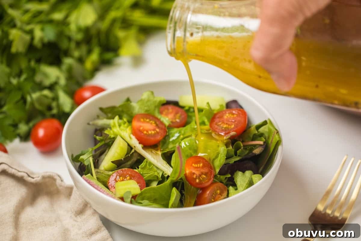 Homemade salad dressing being drizzled over mixed greens salad.