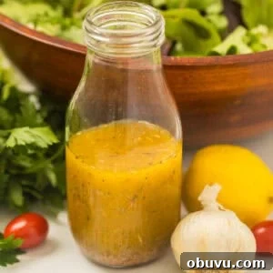 Bottle of homemade zesty Italian dressing next to garlic and a tossed salad.