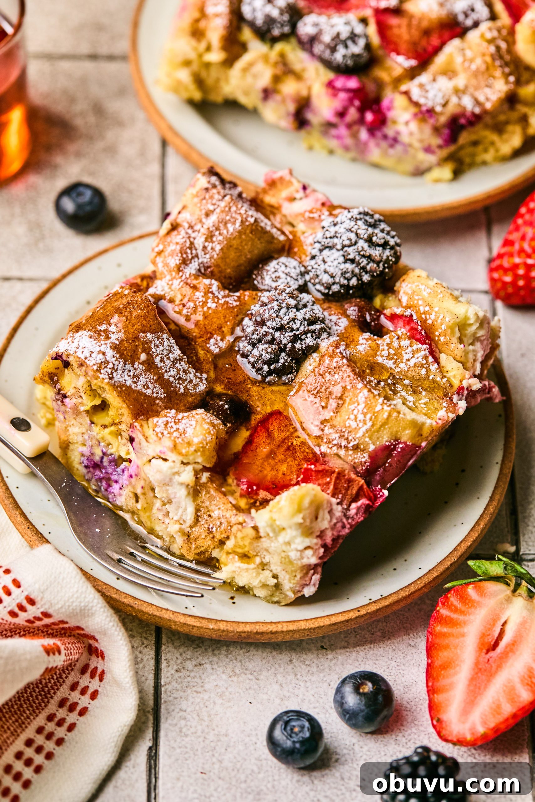 Berries and Cream French Toast Casserole Recipe 9 A slice of berries and cream french toast casserole sitting on a small serving plate next to fresh strawberries, blackberries and blueberries