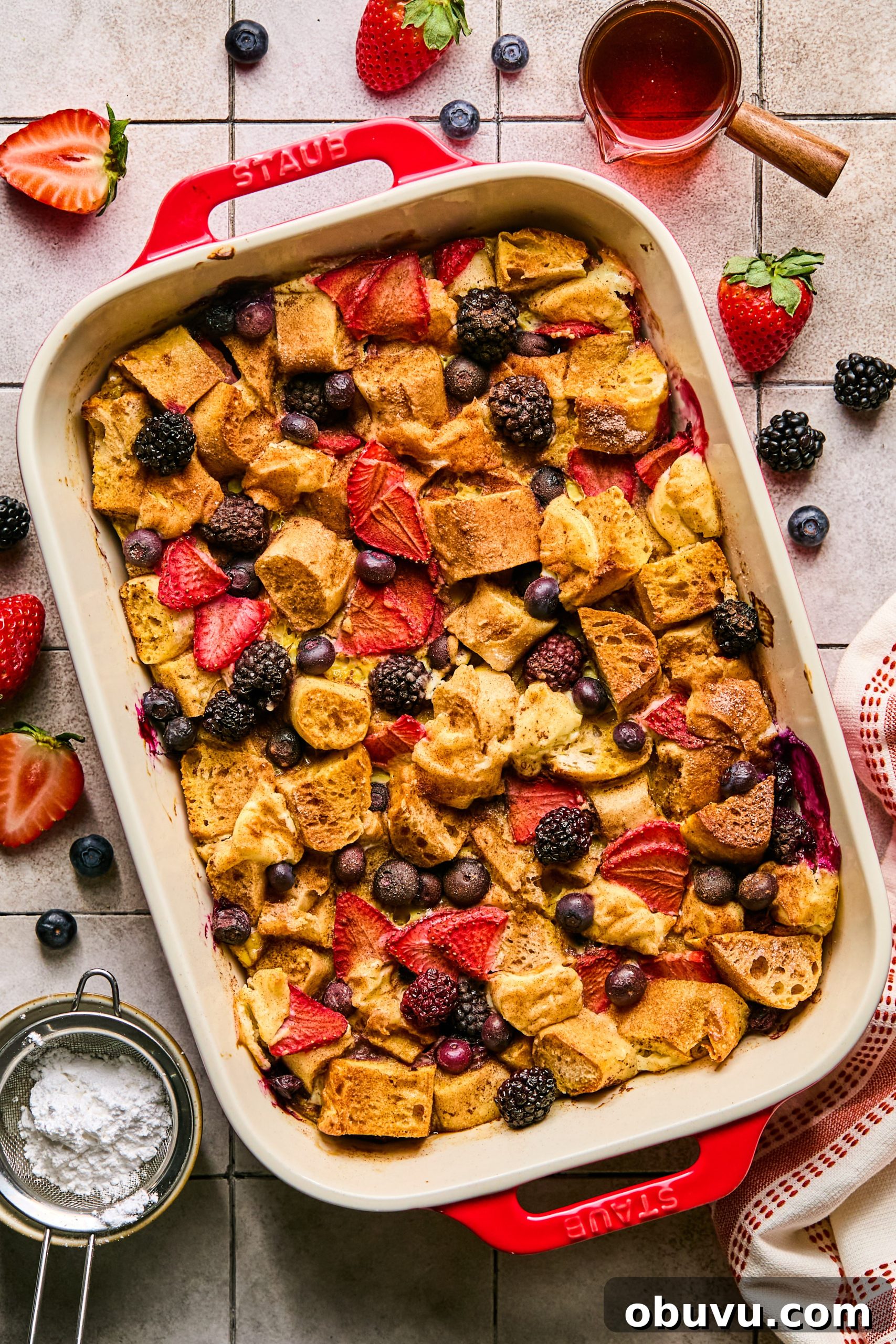 Berries and Cream French Toast Casserole Recipe 10 A mixed berries and cream french toast casserole surrounded by a small jar of maple syrup, powdered sugar, fresh strawberries and blueberries