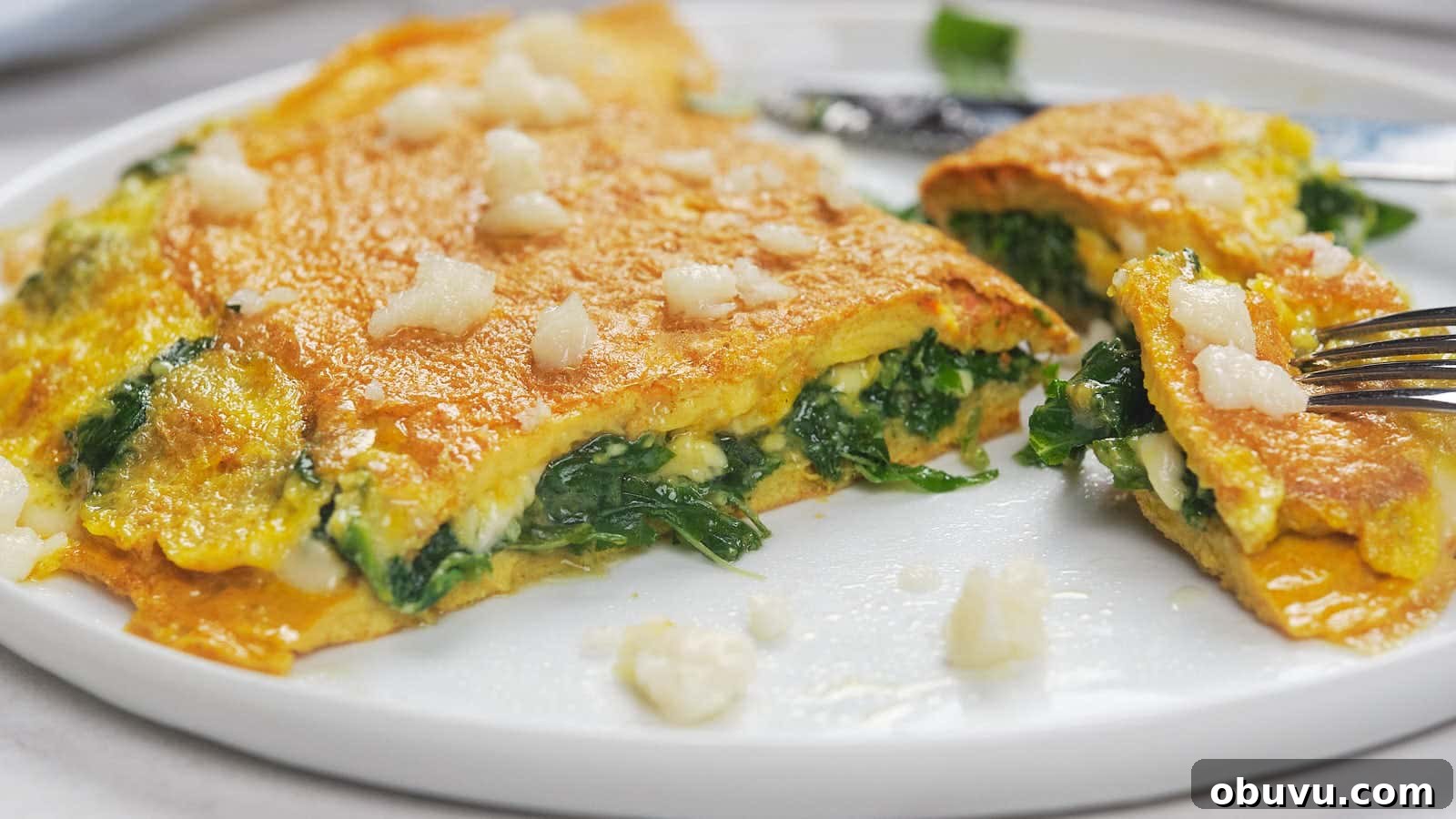 19 Cozy Low-Carb Breakfasts You’ll Crave Every Morning 13 A spinach and cheese omelette is partially sliced on a white plate.