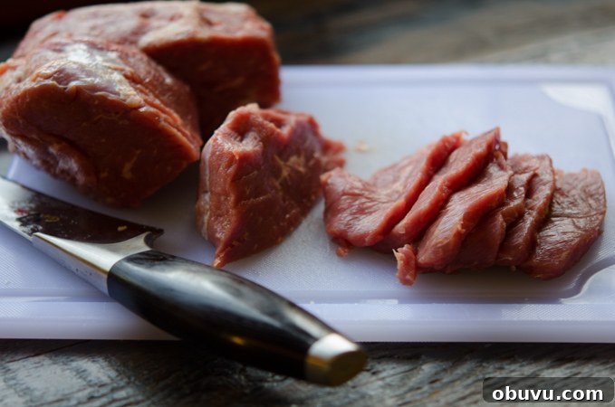 Chinese Beef and Broccoli Stir-Fry Recipe with Savory Sauce 4 A chunk of lean beef thinly sliced on a white cutting board.