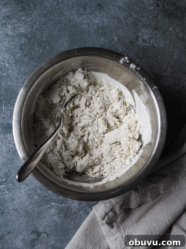 Metal bowl of flour being mixed with water using a fork.