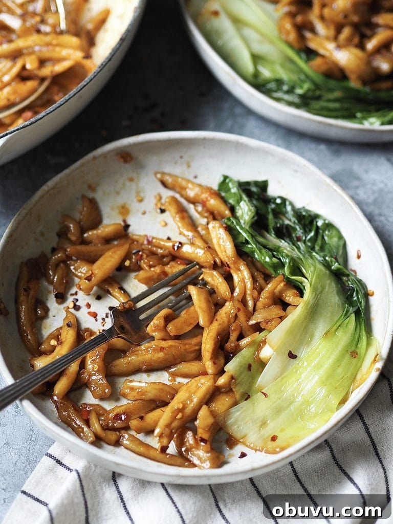 A half eaten bowl of spicy scissor-cut noodles with some wilted pak choi on the side.