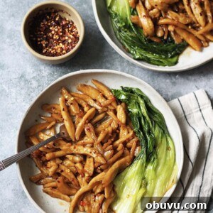 Two plates of scissor cut noodles in chilli oil with pak choi on the side.