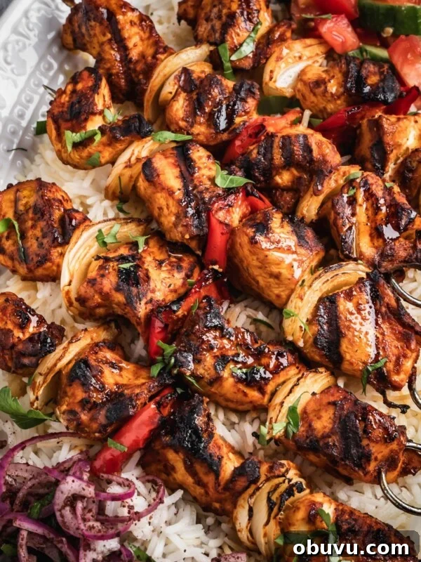 A platter with rice, chopped salad, sumac onions and harissa chicken skewers.