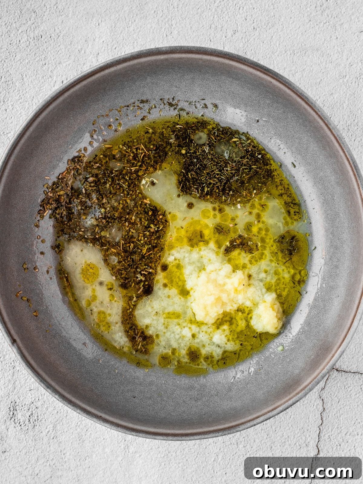 Recipe step showing the preparation of the marinade by mixing the olive oil, lemon juice, garlic and herbs.