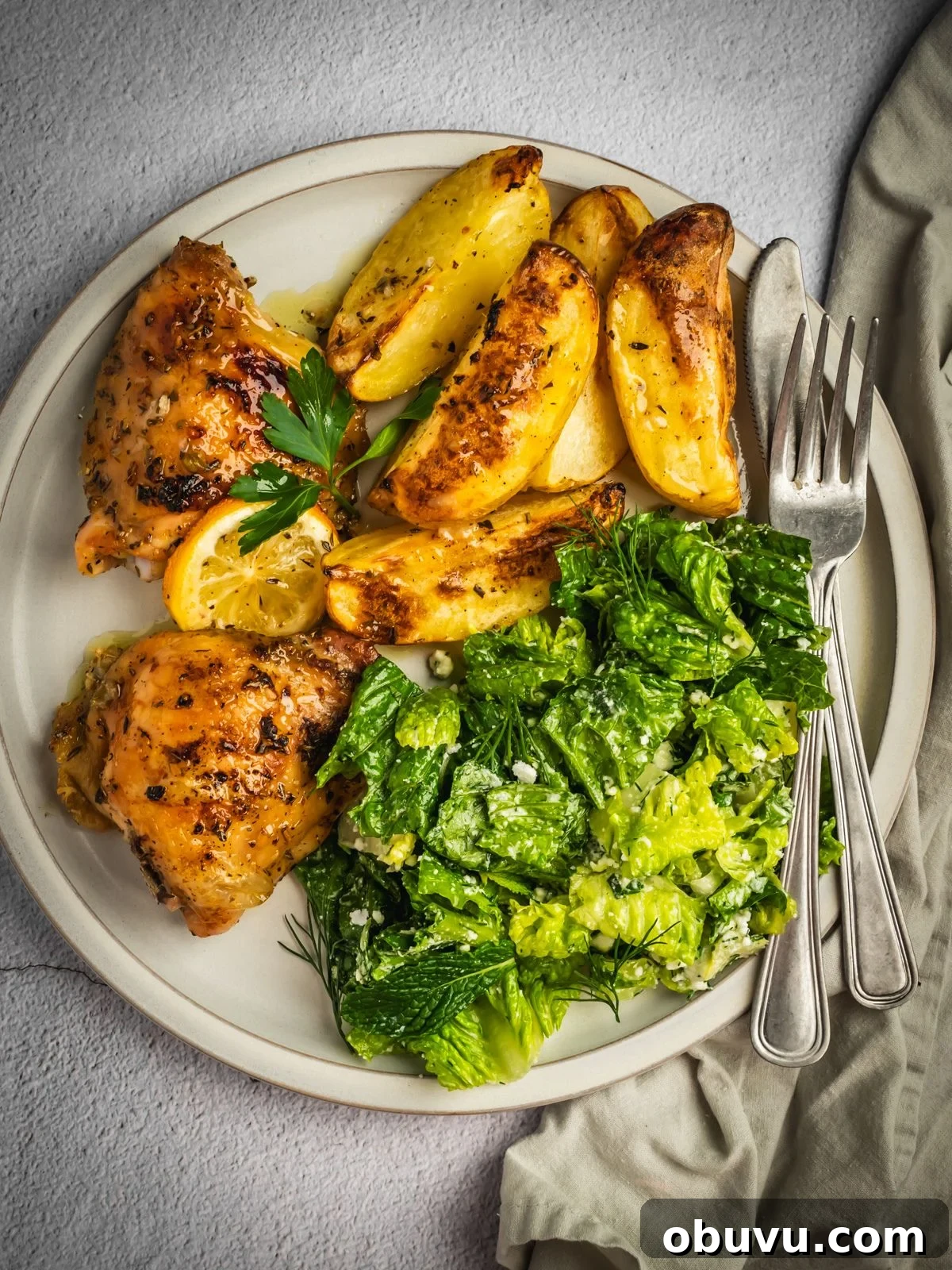 A serving of Greek lemon chicken and potatoes on a plate with a side salad.