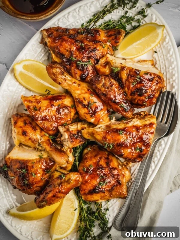 Harissa honey chicken pieces on a platter with fresh thyme and lemon wedges.