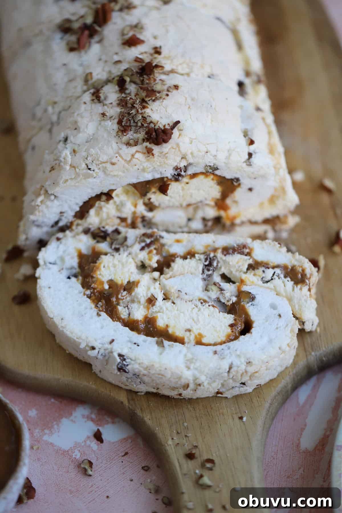 A toffee and pecan meringue roulade on a wooden board.