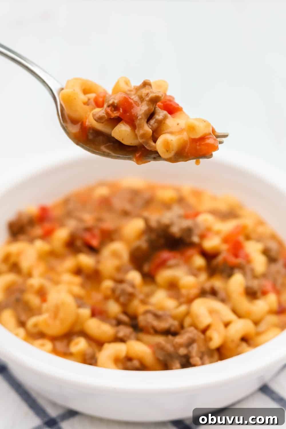 a fork lifts a bite of cheeseburger macaroni made in the Instant Pot out of a bowl serving the same.