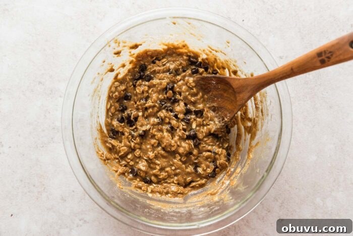 Chocolate chip oatmeal cookie bars batter in a glass mixing bowl with a wooden spoon in it.