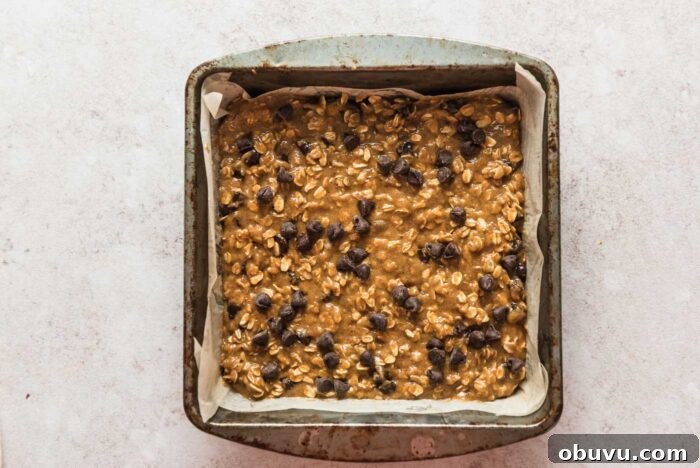 Raw chocolate chip oatmeal cookie bars batter in a baking dish lined with parchment paper.