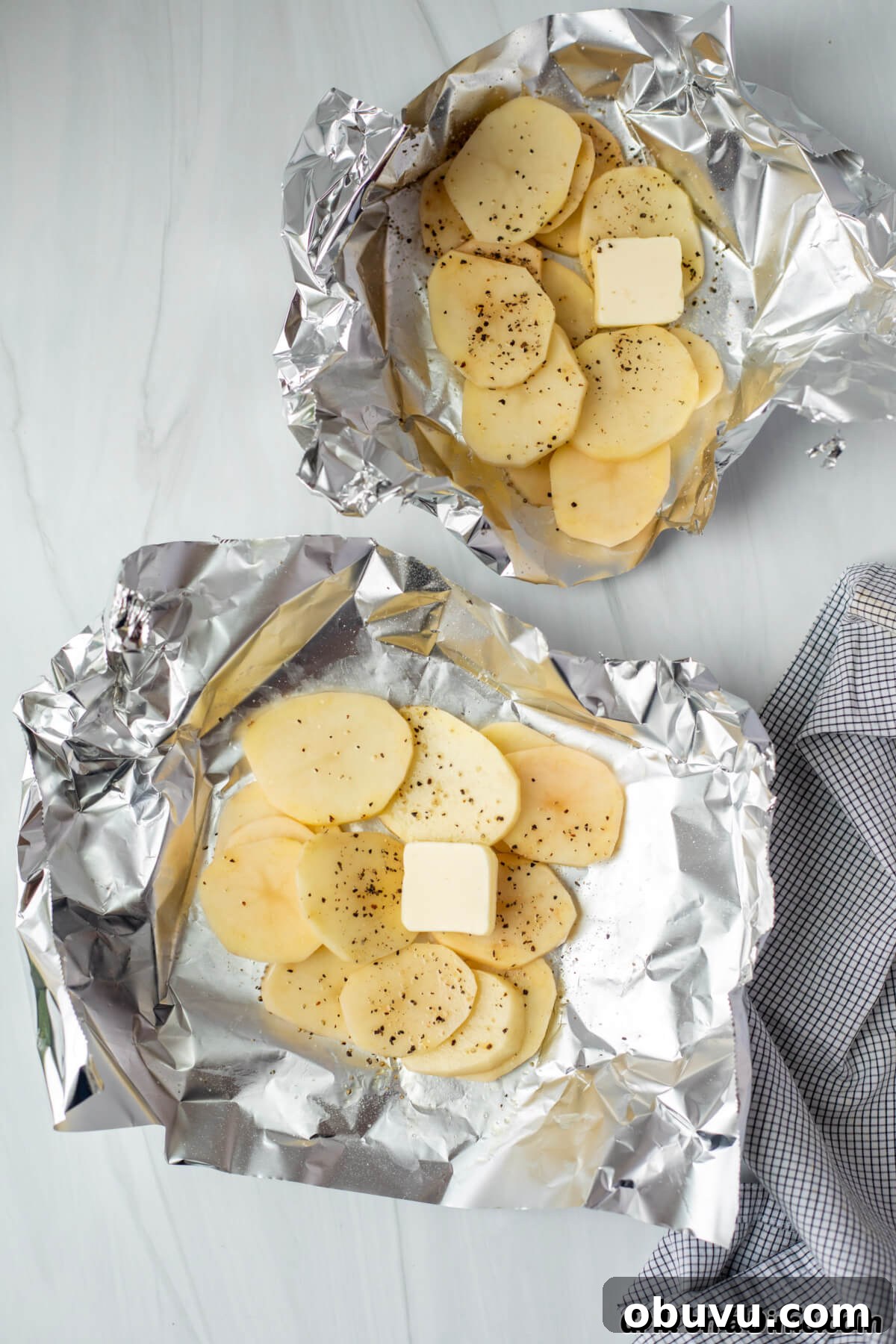 Slice potatoes topped on pieces of foil topped with salt, pepper, and slice of butter